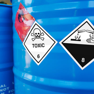 Blaue Chemiefässer mit Gefahrgutaufklebern für entzündbare Stoffe (Klasse 3), giftige Stoffe (Klasse 6) und ätzende Stoffe (Klasse 8).